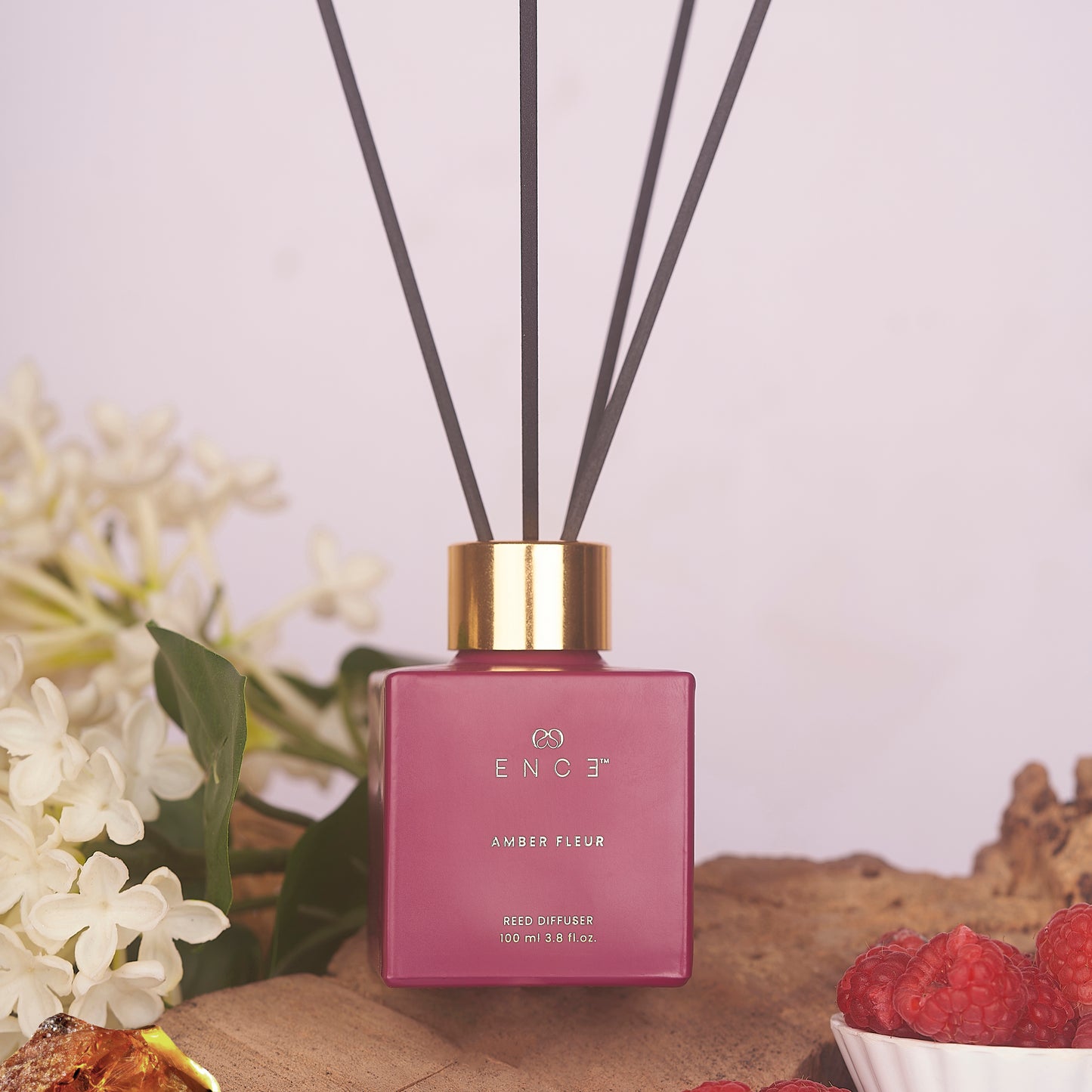 Pink diffuser with gold cap on a wooden surface with flowers and berries in the background