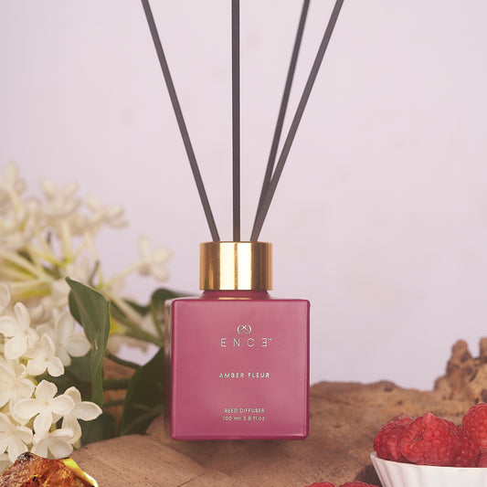 Pink diffuser with gold cap on a wooden surface with flowers and berries in the background