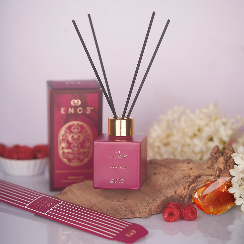 Pink diffuser with black sticks on a wooden surface with flowers and berries.