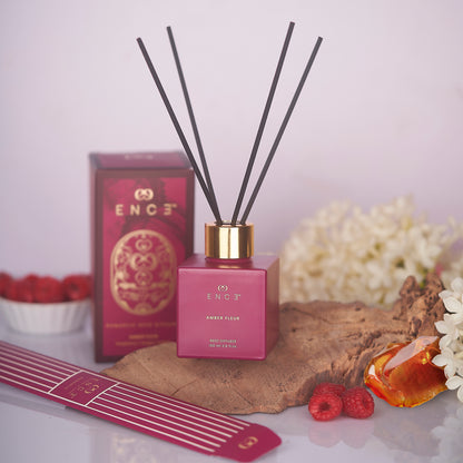Pink diffuser with black sticks on a wooden surface with flowers and berries.